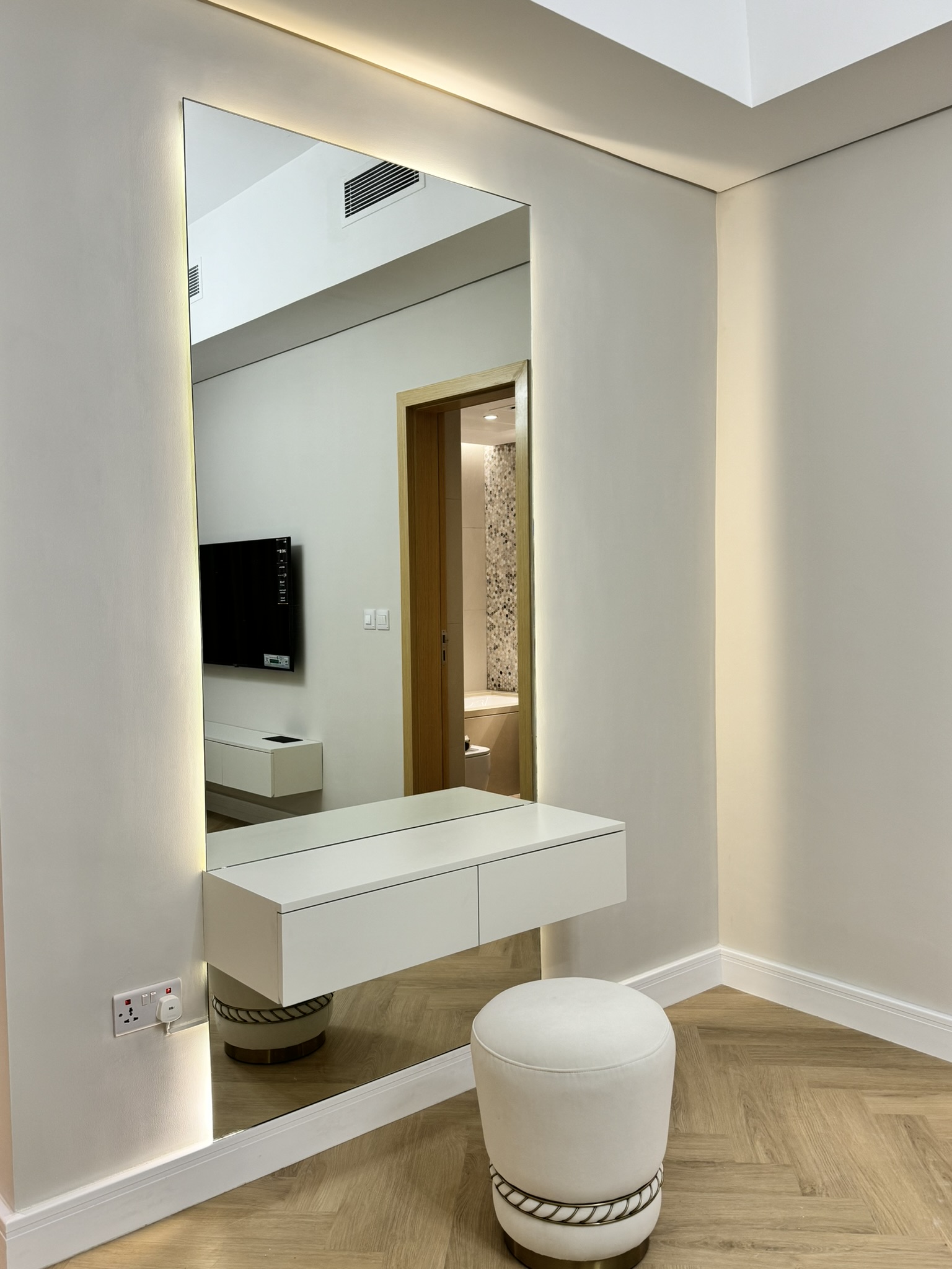 Illuminated mirror above a floating dressing table and round stool at Lisa Villa